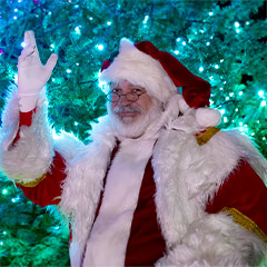 Santa waving with a brightly lit tree behind him